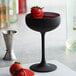 A Stolzle matte black coupe glass with a strawberry in it.