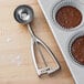 A Vollrath stainless steel ice cream scoop in a cupcake tin with chocolate.