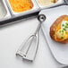 A baked potato with cheese and green onions with a Vollrath stainless steel disher on top.