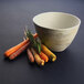 A hand holding an Elite Global Solutions Santiago sandstone bowl filled with carrots and squash on a table.