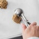 A hand using a Vollrath stainless steel disher to scoop cookie dough.