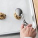 A hand holding a Vollrath stainless steel oval scoop with a cookie on a tray.
