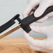 A person in gloves using a Mercer Culinary serrated knife with a black handle.