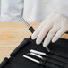 A hand in white gloves holding a Mercer Culinary garnish tool set.