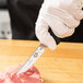 A person in gloves using a Victorinox poultry boning knife to cut meat.