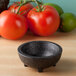 A black charcoal polypropylene Pequeno molcajete on a wood surface with tomatoes and a lime.