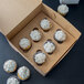 A Kraft cupcake box with 6 cupcakes with white frosting.