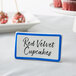A blue ceramic table tent sign with a blue decal border on a table with red and white objects.