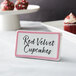 A ceramic table tent sign with a rose decal border on a counter with a sign that says "red velvet cupcakes"