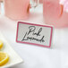 A Choice ceramic table tent sign with a rose decal border on a table with a plate of lemonade with a pink rose decal border.