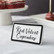 A black ceramic table tent sign with red text on a table.