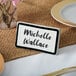 A black ceramic table tent sign with a black decal border and the name "Michelle Wallace" on it.