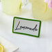 A table tent sign with a green border on a table with lemons and cups of liquid.