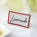 A maroon ceramic table tent sign with a red border on a hotel table next to a plate of lemons.