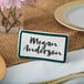 A teal ceramic table tent with a white and green border and the name "Megan Anderson" on it.