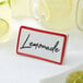 A red ceramic table tent sign with a lemon border next to a plate of lemons.