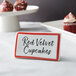 A red ceramic table tent sign with a border displaying red velvet cupcakes on a table