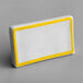 A white rectangular ceramic table tent sign with a yellow border.
