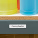 A shelf with a white rectangle label on a blue container of cleaning supplies.