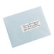 A blue envelope with a close-up of a white Avery rectangle label with black writing on it.