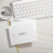 A white desk with a white keyboard and Avery silver rectangle foil return address labels on white envelopes.