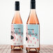 Two white Avery mailing labels on wine bottles with pink liquid.