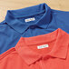 Two polo shirts, one blue and one orange, each with a white rectangular fabric label with a name written on it.