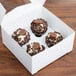 A white 8" x 8" x 4" auto-popup window cupcake box with chocolate peanut butter cupcakes and chocolate curls.