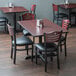 A Lancaster Table & Seating dining set with mahogany bistro chairs and padded seats next to a table.
