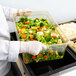 A person in white gloves holding a Cambro container of broccoli and carrots.