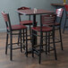A Lancaster Table & Seating bar table with a cherry top and black base with mahogany chairs.