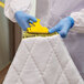 A person in a white suit and blue gloves using a yellow Rubbermaid biohazard mop pad to clean a mattress.