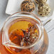 A glass teapot with Numi Petite Bouquet Flowering Tea Blossoms steeping inside.
