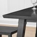 A Lancaster Table & Seating live edge bar height table with an antique slate gray finish with a wine glass on it.