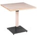 A Lancaster Table & Seating square wood table with a metal base.