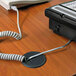 A telephone cord is attached to a black Master Caster Cord Away grommet in a desk.