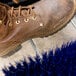 A brown boot on a blue Carlisle shoe brush with metal foot.