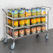A Regency stainless steel utility cart filled with canned and jarred food.