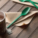 A green EcoChoice Heavy Weight CPLA plastic spoon on a napkin next to a regular spoon.