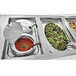 A Vollrath slotted hinged stainless steel cover on a buffet tray with food.
