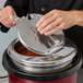A hand using a Vollrath slotted hinged lid to cover a stainless steel pot.
