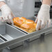 A person in white gloves placing a loaf of bread into a Chicago Metallic aluminized steel bread loaf pan.