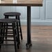 A Lancaster Table & Seating black cast iron counter height end column table base on a wood surface with stools