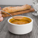 A Oneida Baguette stainless steel bouillon spoon holding soup over a bowl of soup.