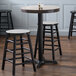 A Lancaster Table & Seating black cast iron counter height table base with three stools at a table.