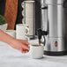 A person pouring coffee into a Waring commercial coffee urn.