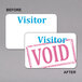 A white visitor badge with blue void stickers.
