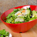A red slanted melamine bowl filled with salad on a table.