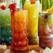A group of colorful drinks in Moai tiki glasses on a table.