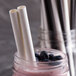A glass jar filled with blueberries and EcoChoice giant white unwrapped paper straws.